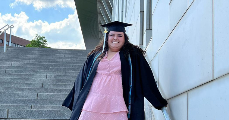Julia Medeiros wearing commencement cap and gown on UMass Boston steps