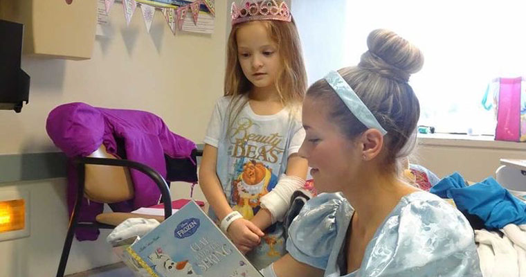 Cinderalla reads a book to a young patient