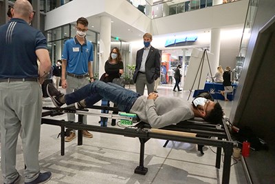 Biomedical engineering majors Steven Evangelos, left, and Mark Elman, second from left, let a student try their 'Alarius Table' during the preliminary round of the DifferenceMaker Prototyping Competition at University Crossing. They won the $2,500 first prize.  