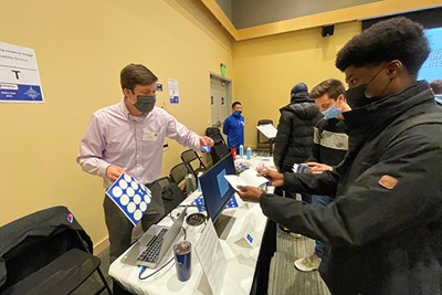 Disability Services Assoc. Director Brandon Drake gives a student a sticker for his Ethics Fest "passport" after visiting the "Exploring Universal Design" station at University Crossing.