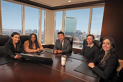 Five UMass Lowell students sit and smile at the camera while sitting in a board room in Boston