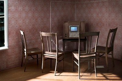 A vintage tv set with four wooden chairs around it sits in a room with pink wallpaper