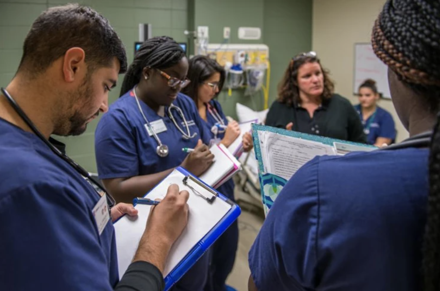 Nursing students write notes while professor speaks to them