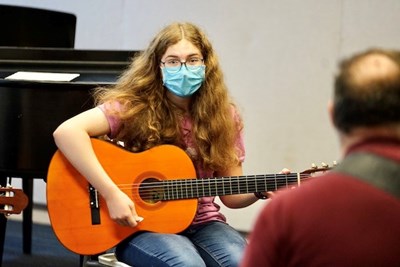 A band camp participant works on her acoustic guitar skills with an instructor.