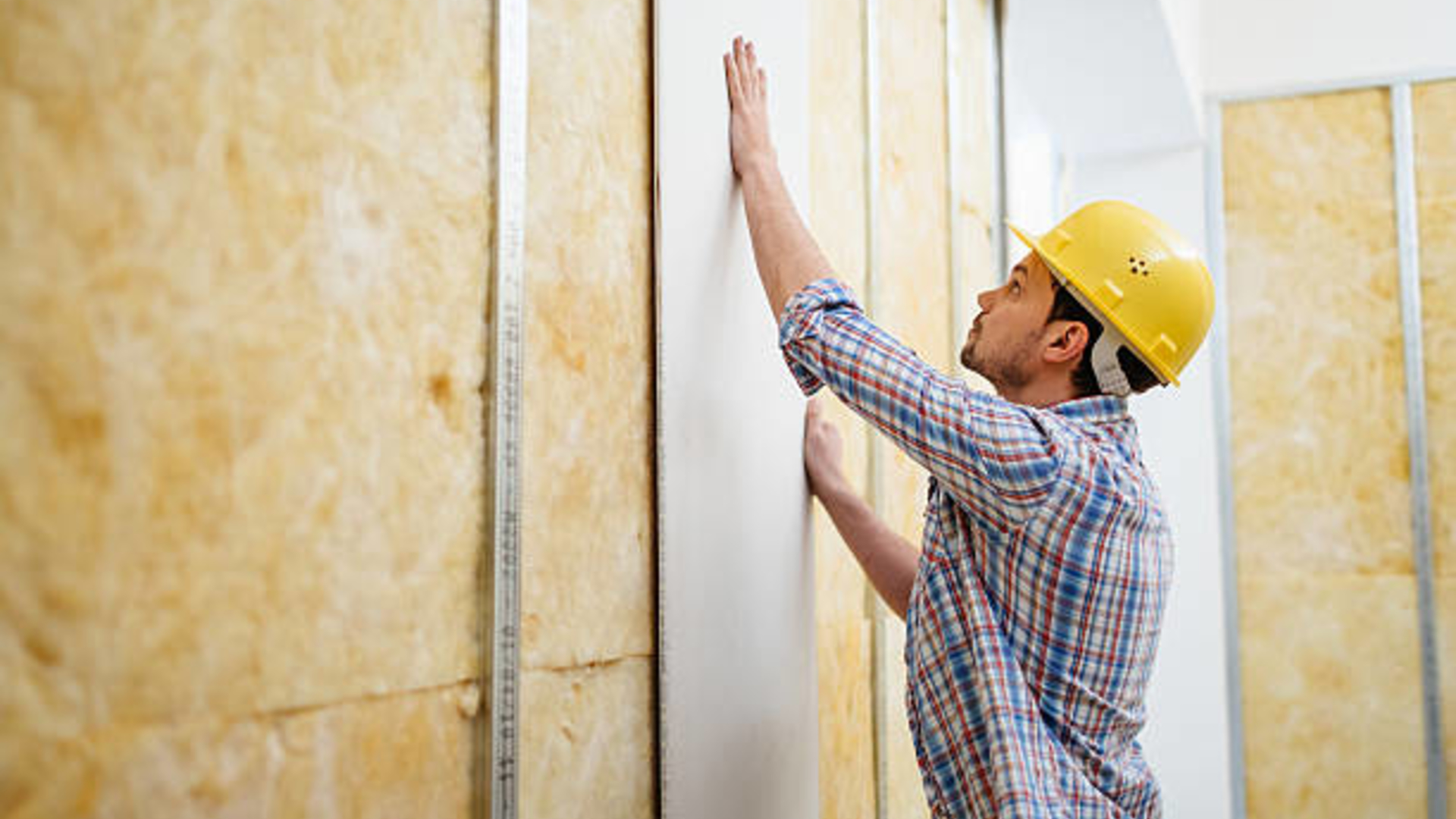 A male construction workers places a board on a wall