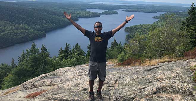 Vinay Sampson stands on top of mountain with arms open